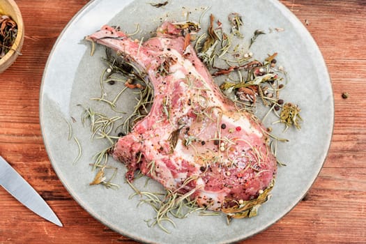 Raw pork steak Tomahawk marinated in spicy herbs on wooden background.