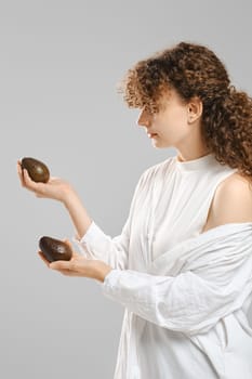 Cute woman looking at two whole avocado in her hands
