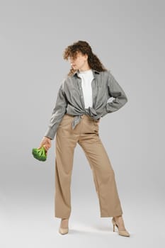 Young woman posing with broccoli in hand in grey studio