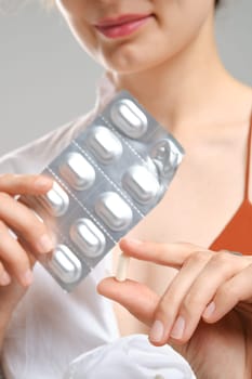 Close up view of fingers holding a pill in front of the package