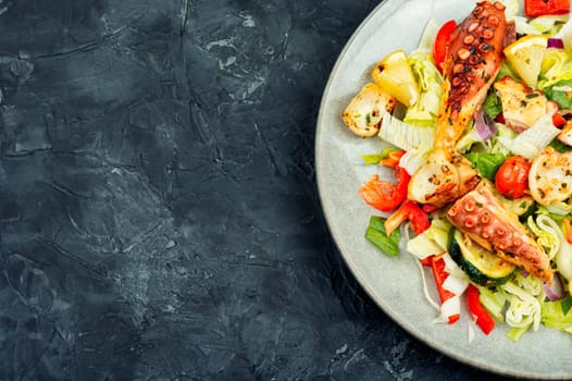 Healthy salad of vegetables and grilled octopus in plate on dark stone table. Space for text