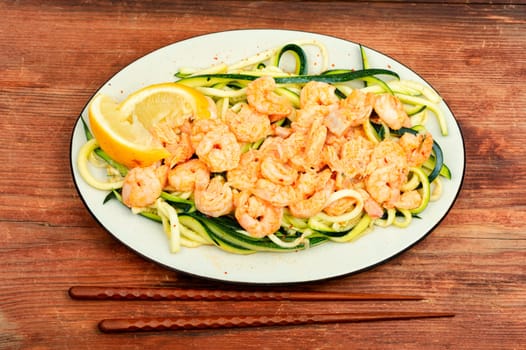 Stewed shrimps with sliced zucchini on rustic wooden table. Top view.
