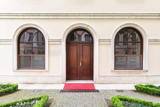 Wooden arched door between two arched windows in a stone wall painted in beige