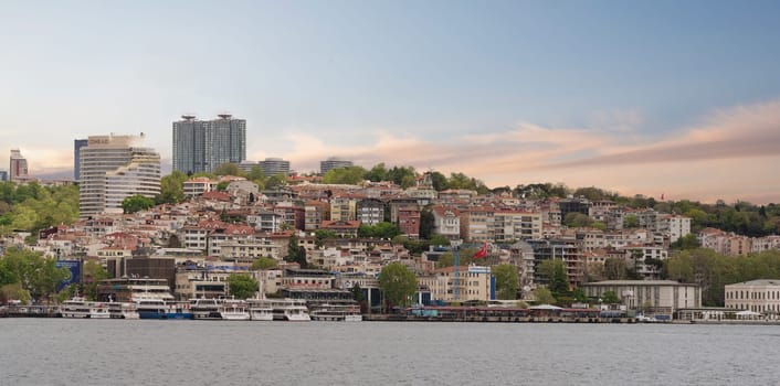 European side of the Bosphorus Strait, Istanbul, Turkey, with a ferry boat floating on the water, and city skyline in the background. The sky is clear, and the water is calm