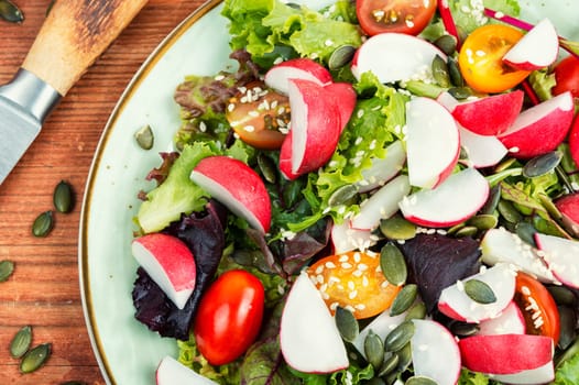 Tasty salad with radish, greens, tomato and sesame. Vegan recipe.