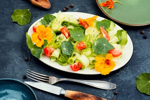 Rural salad with vegetables, nasturtium and dressing on wooden table.
