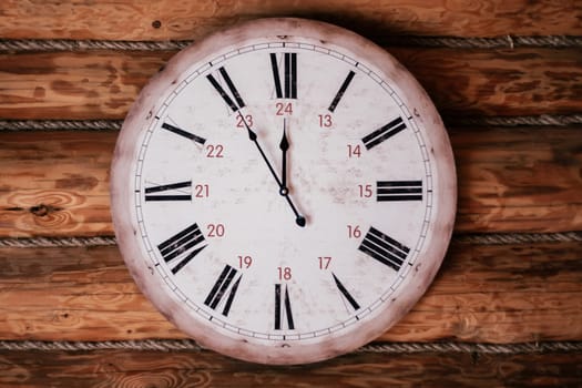 Round vintage clock showing five minutes to noon, midnight hangs on wooden wall. Decorative elements. Countdown. Design. Cozy house . Retro style. Sense of time. Space for text.