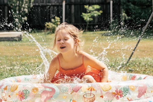 Little girl having fun splashing water in inflatable pool on summer day outside. Games and entertainment. Summer holidays. Happy childhood.Happy summer days. Positive emotions.