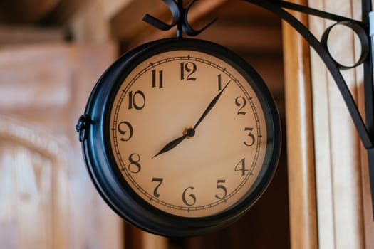 Round vintage clock in black metal hanging on corner mount on wooden wall. Decorative elements. Countdown. Design. Retro style. Sense of time. Round clock signboard. Mock up Round shape.