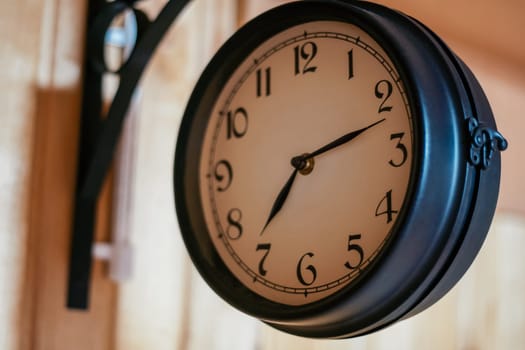 Decorative elements. Round vintage clock in black metal hanging on corner mount on wooden wall. Countdown. Design. Cozy house . Retro style. Sense of time. Round clock signboard.