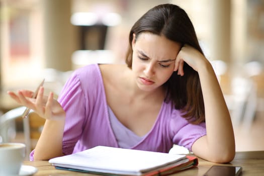 Confused student checking lesson on notebook in a bar terrace