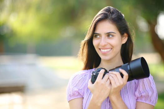 Happy photographer looking at side holding camera in a park