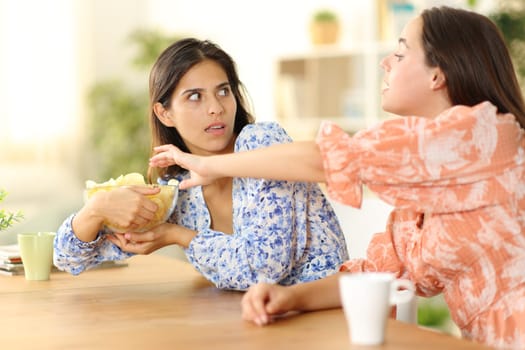 Woman trying to eat potatto chips and selfish friend avoiding at home