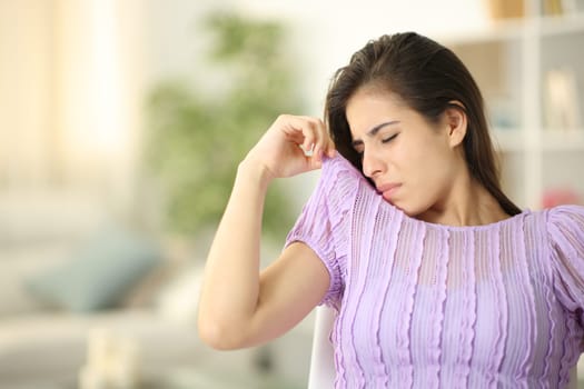 Woman smelling her stinky clothes sitting at home