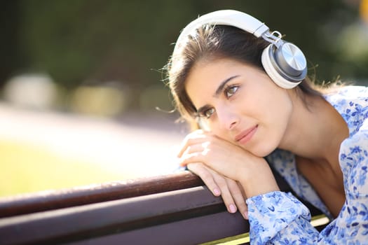 Pensive woman listening audio with headphone in a park
