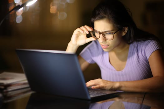 Woman using eyeglasses forcing sight with laptop in the night at home