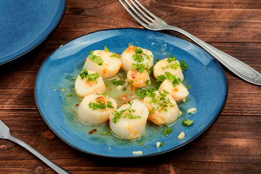 Roasted scallops with green, grilled sea scallops in creamy sauce. Wooden background.