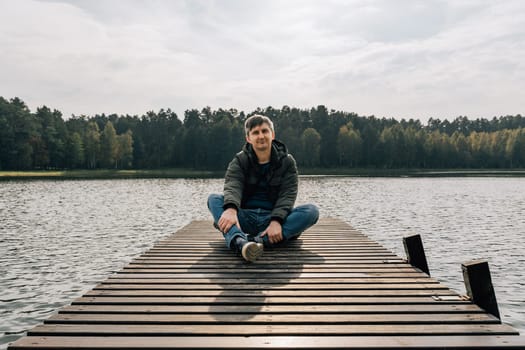 A man enjoys a sunny autumn day while sitting on a wooden pier on a lake.