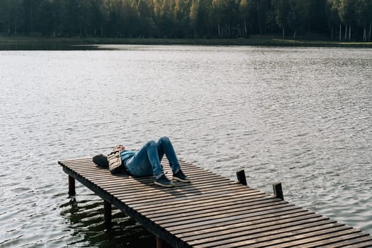 A man relaxes lying on a wooden boat dock on a lake in autumn.