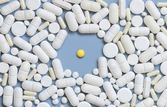 Mix of white medical capsules and pills with one yellow pill in the middle on light blue top view. Medicinal treatment. Taking dietary supplements and vitamins. Assorted pharmaceutical products
