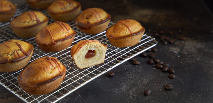 Pasticciotto leccese pastry filled with egg custard cream and sour cherry jam, typical apulian breakfast, close up. Whole and half pasticiotties on a cooling backing rack on a dark table, copy space