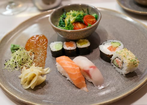 A plate with salad and sushi rolls, fresh raw fish.