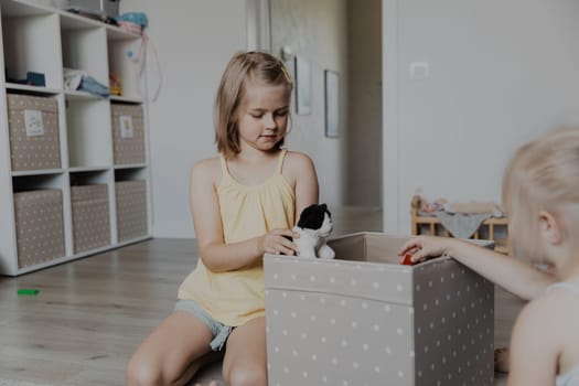 Children cleaning toys from floor after playing, collect them to textile box. Kids sitting on carpet at white home bedroom, kindergarten playroom or playground center. Educational eco-friendly games
