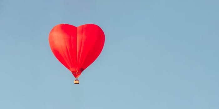 Red Hot air balloon in shape of heart in a blue sky. Space for text. Evening light