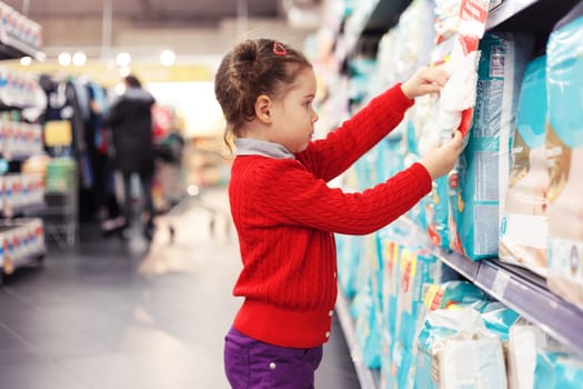 Little girl selects diapers in supermarket.