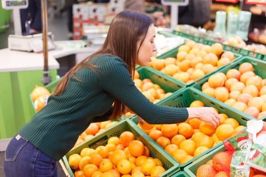 A young woman in a store chooses oranges