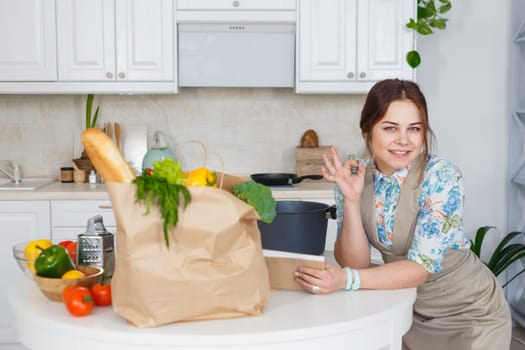 Young housewife gesturing ok with recipe book at the kitchen
