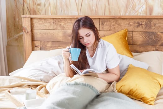 Cute girl on a comfortable chair with tea ,reading a book, the concept of comfort and hipster.
