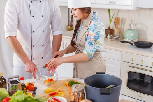 Cook in uniform and his apprentice cooking vegetarian meal