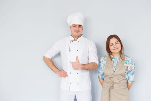 Chef men and woman wearing apron isolated on light background. Couple at work. Thumb up.