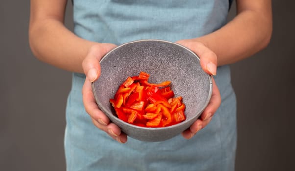 Red sliced pepper pieces in a bowl, prepare healthy food with paprika vegetables, holding fresh organic nutrition in the hands