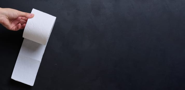 A female hand holds a roll of white toilet paper against a black background. Copy space