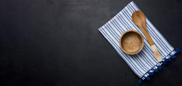 Empty bowl and wooden spoon on a black table, top view. Copy space