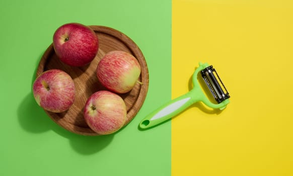 Red apples and peeler on green background, top view