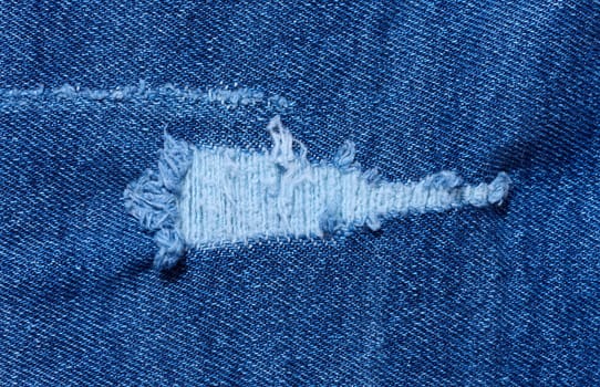 Fragment of blue jeans fabric with a hole, full frame, close up