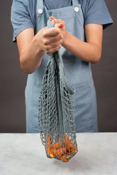 Holding fresh carrots in a reusable grocery mesh bag, vegetables from the market, healthy food and zero waste
