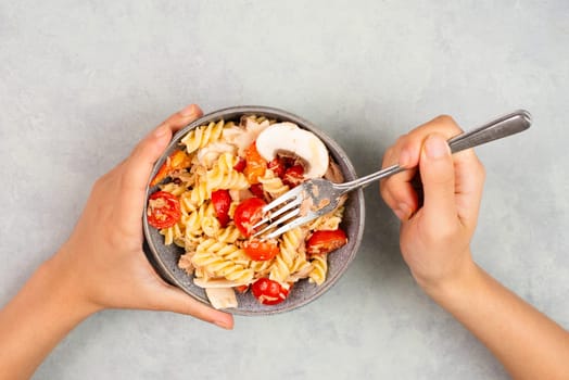Eating a pasta salad with sliced mushroom, tomato, red pepper pieces and tuna, healthy food with vegetables, fresh organic nutrition