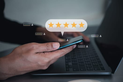 Man using smartphone and laptop computer to rate and evaluate services, with a popup five star icon for good feedback review. Business and technology concept with digital marketing