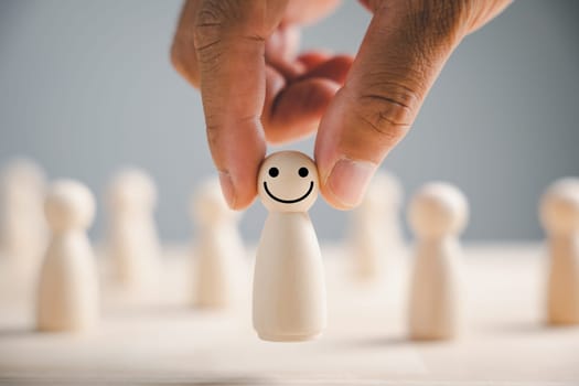 Wooden figure with happy face hand picked from crowd. Customer service rating experience feedback. HR management choosing positive leader to motivate team towards satisfaction and success in business