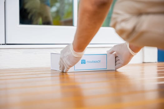 Delivery hands with gloves transport holding medication package box first aid shipment from pharmacy hospital delivery on floor at door front home patient, Buy online clinic retail Rx drug store