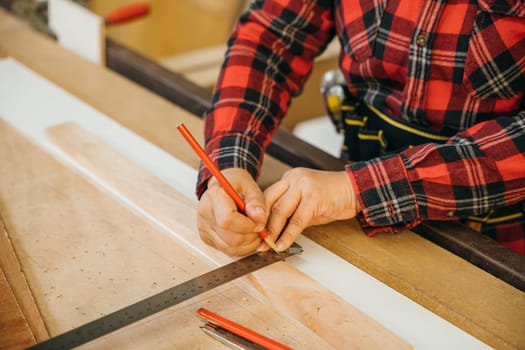 Asian senior woman carpenter taking measurement of a wooden plank and make in workshop, female holding ruler and pencil while making marks on wood at woodshop, Happy carpenter day