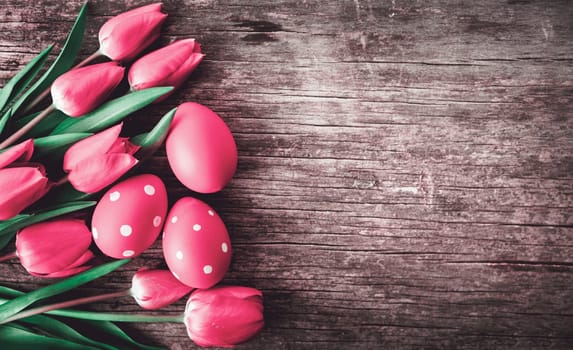 Red easter eggs and pink tulip flower on vintage wooden table from above. Easter holiday and springtime background design. Top view.