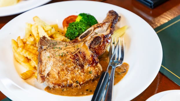 A plate of pork steak was cooked medium rare. Golden fried potatoes Broccoli and tomatoes are the side vegetables. This picture was taken from the restaurant. Suitable for eating as a main course.