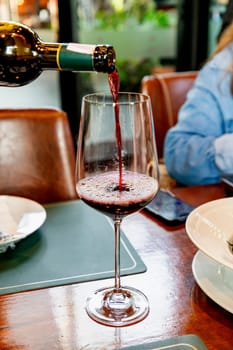 A waiter in a restaurant is pouring wine into wine glasses on a table at a party. There are blurry people attending the event in the background, conveying a relaxed and cheerful atmosphere.