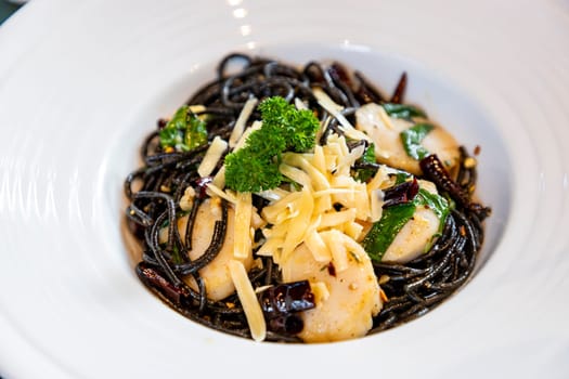 Spaghetti with scallops and sprinkled with cheese in a white plate. The black spaghetti has a slightly salty and spicy taste. Scallops are sweet and nutty. The cheese is salty and oily, so it's mellow