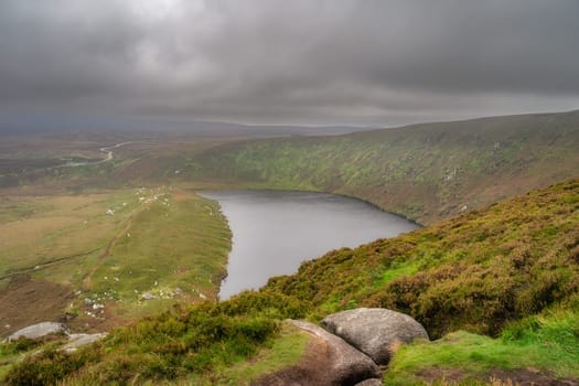 View on the lake Lough Bray from the top of the hill, covered in moody, dramatic storm clouds. Hiking in Wicklow Mountains, Ireland